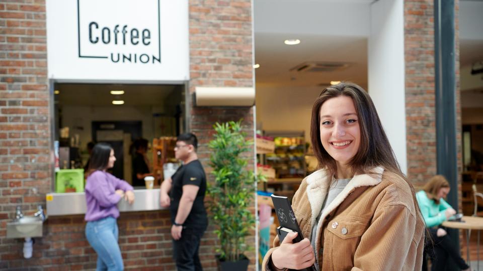Student standing in front of Coffee Union holding books and smiling