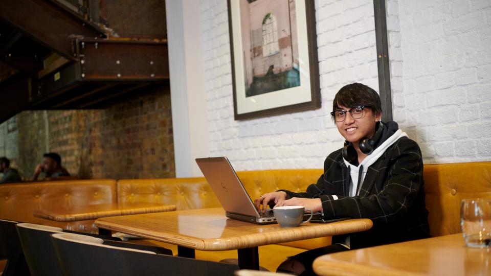 Student working on a laptop with headphones in a cafe