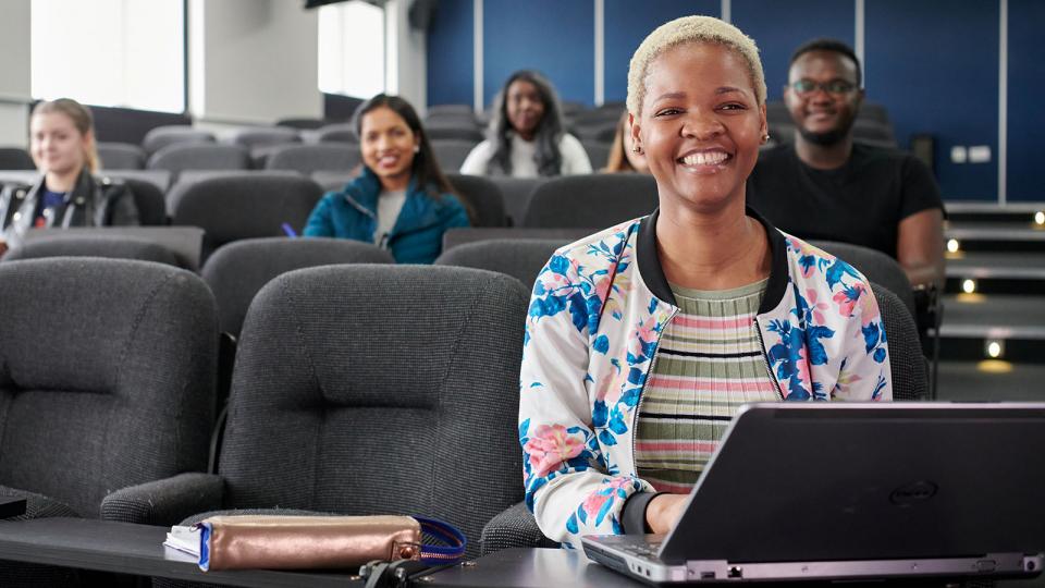 A woman smiling whilst at her laptop during a lecture.