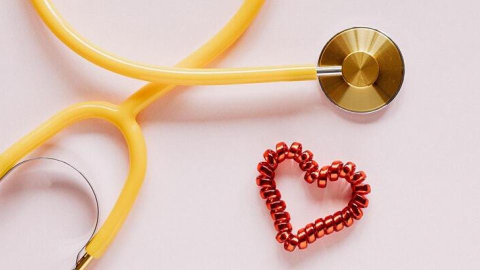 A yellow stethoscope on a white background with a hair tie in the shape of a heart next to it