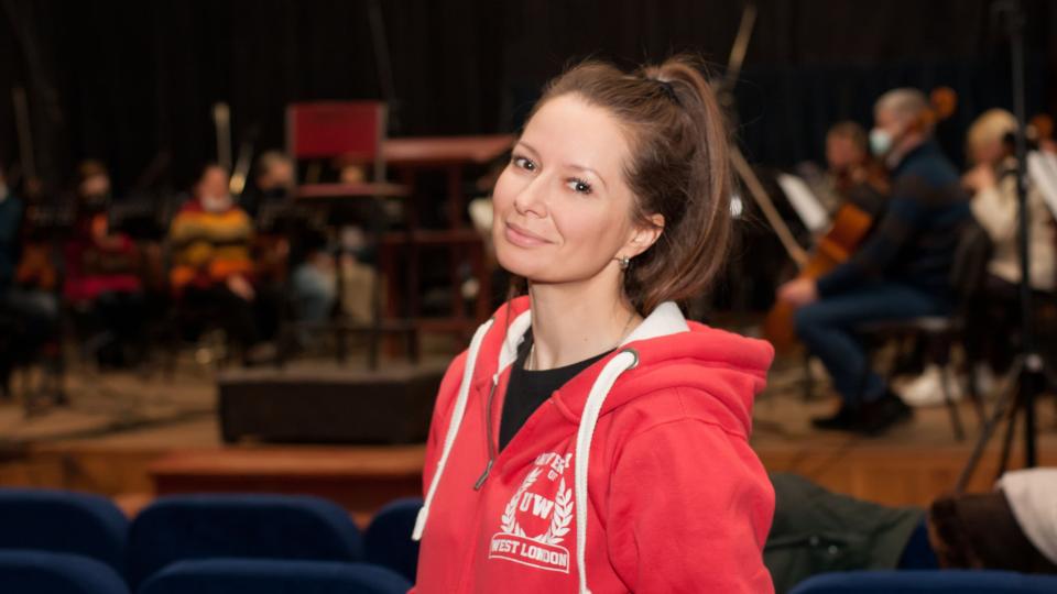 Iryna Gould wearing a red hoodie standing in front of the orchestra