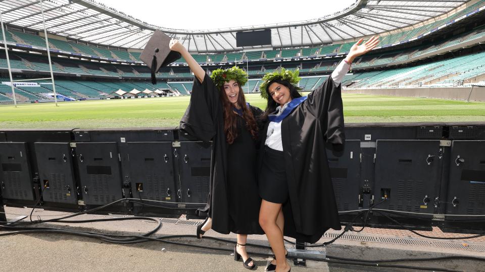 Two graduands posing pitchside at Twickenham Stadium. 