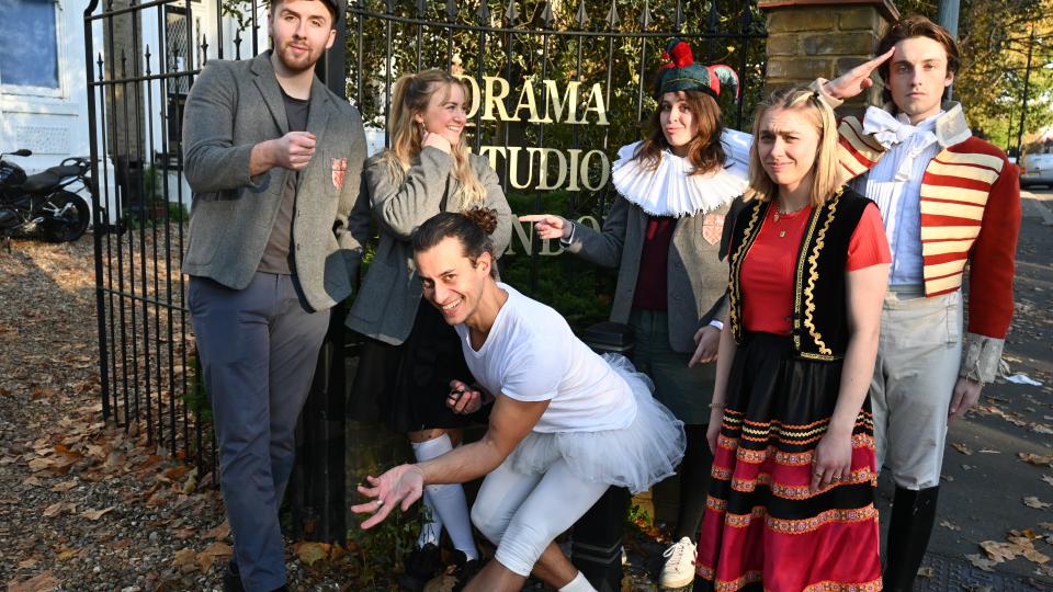 A group of Drama studio london students are dressed up in panto costumes ready to perform the steadfast tin soldier. They are stood in front of the drama studio london gate.