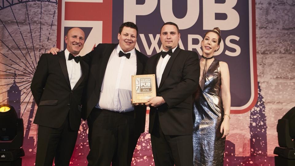 Chris Hurter receiving an award on stage at The Great British Pub Awards 2016, dressed formally, with three others present including Katherine Ryan.