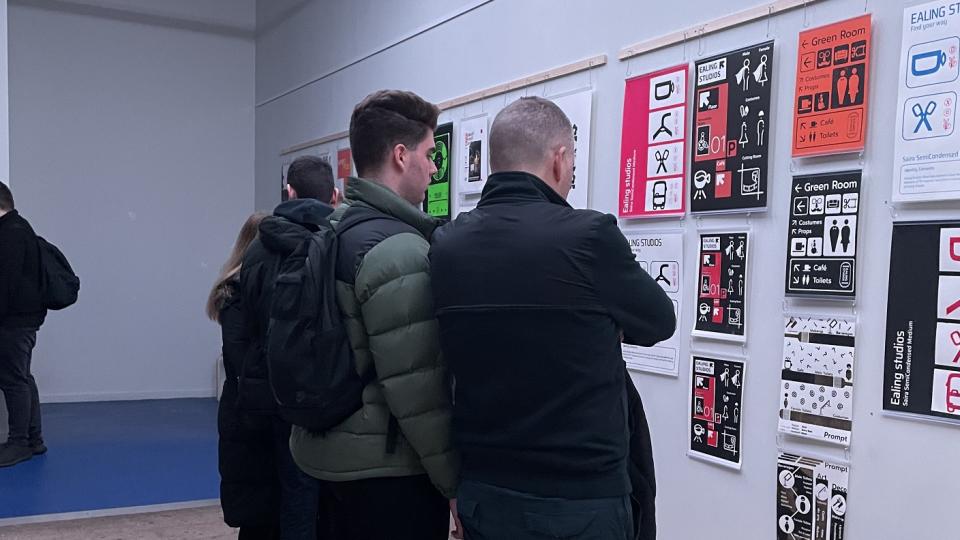 Two men look at colourful graphic design work in an exhibition space