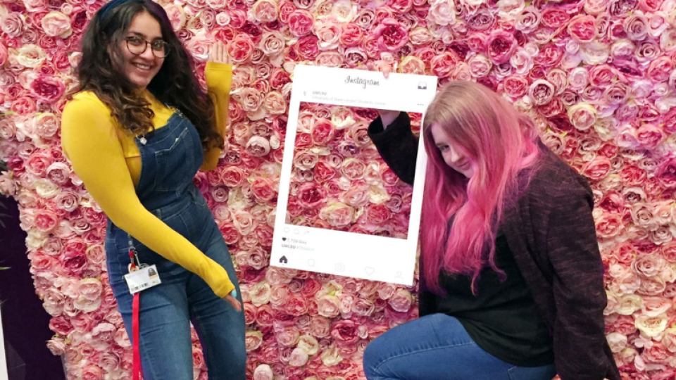 Daniya Kayani posing with an Instagram feed cutout in front of a wall of flowers