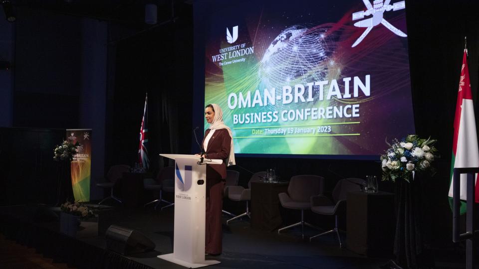 Minister Plenipotentiary Arwa Al-Bulushi at Oman-Britain Business Conference talking to room at UWL with Oman-Britain Business Conference projected behind her.