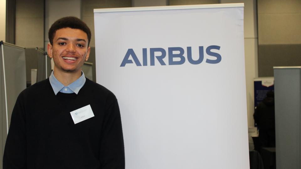 Irvine, student at UWL, wearing a dark jumper with short brown hair, is standing next to the AIRBUS logo.