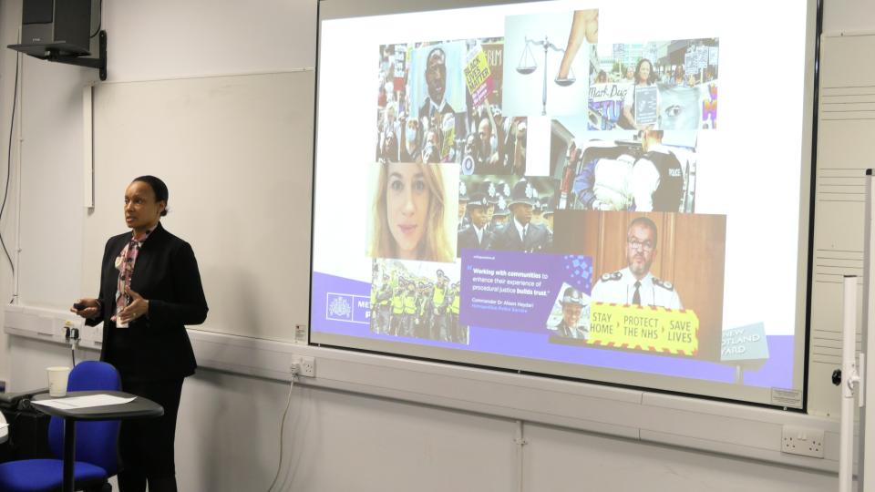 A speaker talking at International Women’s Day Conference with the Metropolitan Police, with a slideshow projected onto the screen behind her.