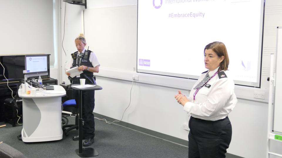 Two speakers from the Metropolitan Police talking at International Women’s Day Conference with a slideshow projected onto the screen behind them.