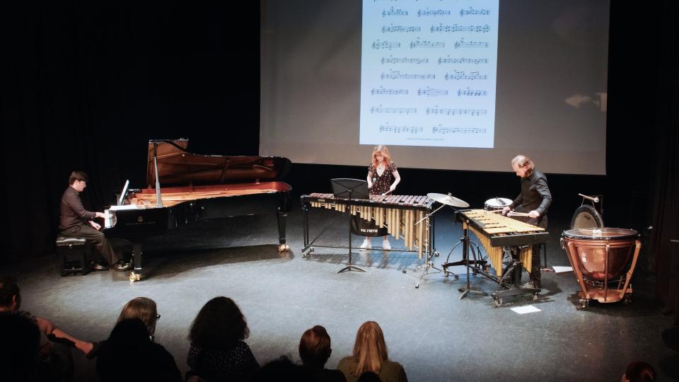 Three LCM musicians onstage performing. They are playing a piano and two xylophones