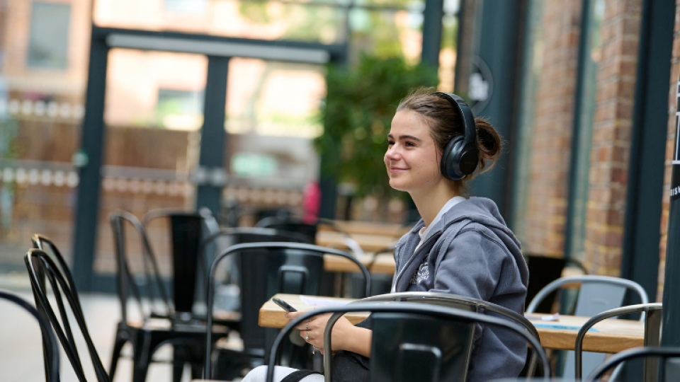 A student seated in Coffee Union smiling whilst listening to music with headphones on.