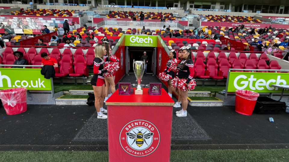 UWL cheerleaders standing in front of a football trophy at the Brentford FC stadium