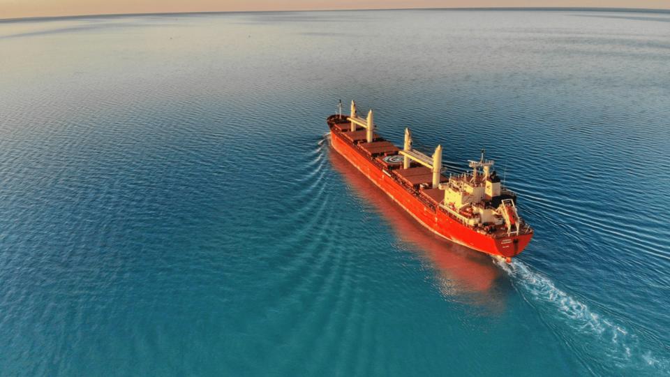 A red cargo ship holding containers travelling across a smooth sea