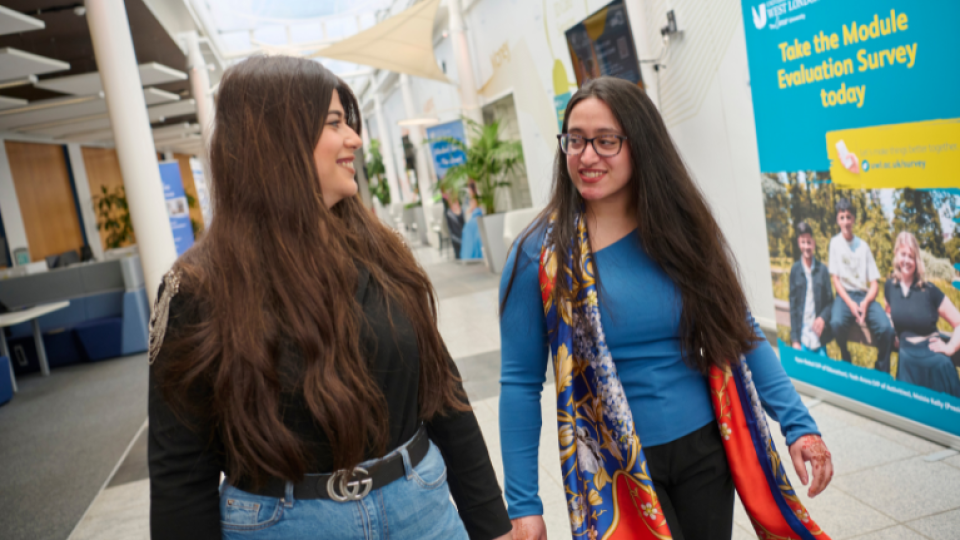 Two students walking through campus, smiling and socialising.
