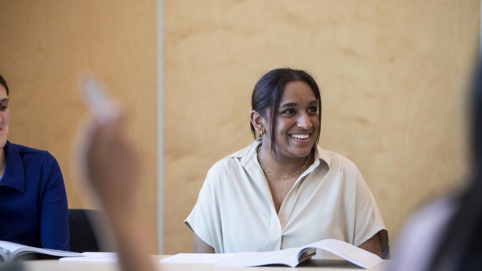 Female student at a desk with a book smiling