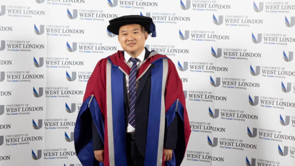 Sam Liu is wearing a gown and hat and is facing the camera.