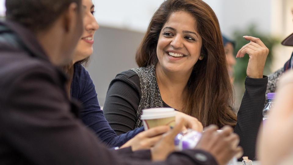 A group of students smiling and having snacks and coffee together at a table.