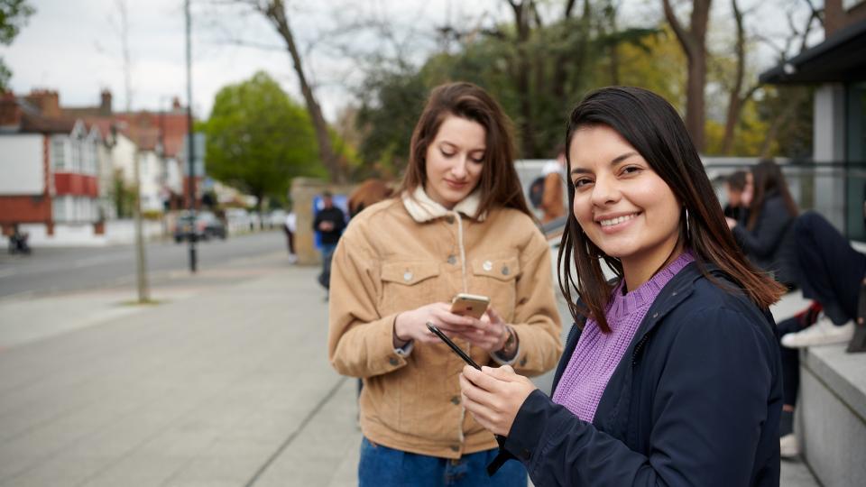 Two students standing outside of UWL (Ealing site), holding their phones.