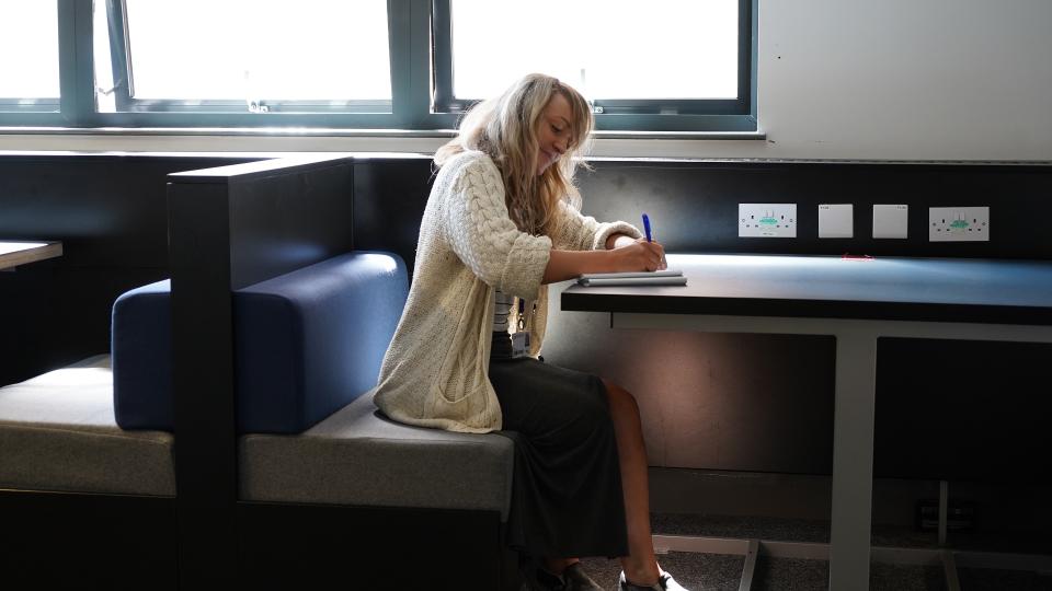 A student studying at a desk in the library next to a window.