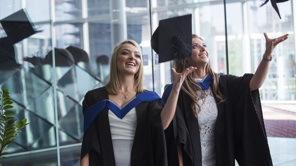 Two students at graduation tossing their caps in the air