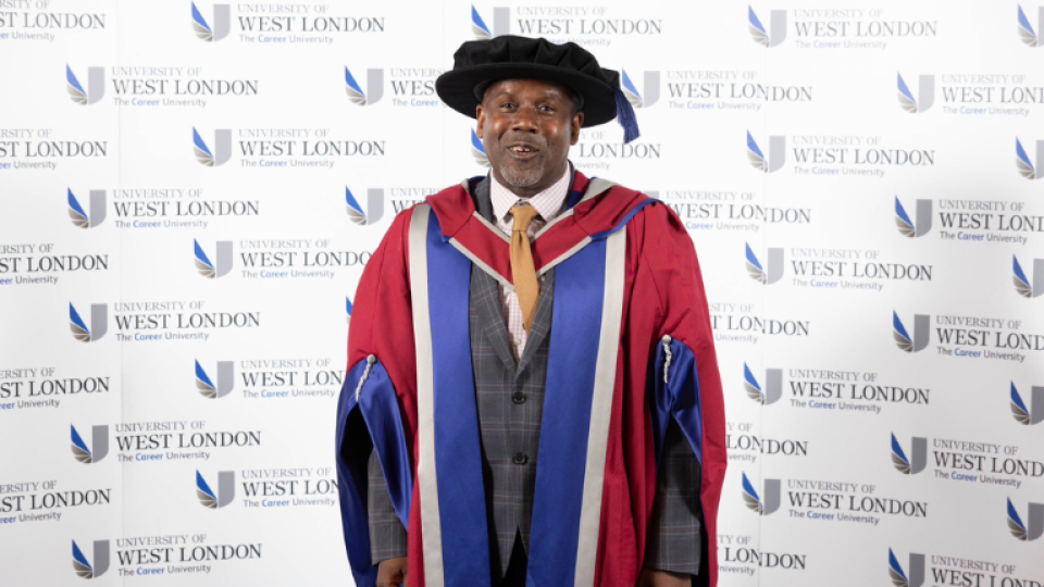 Lee John Charles CBE is wearing a gown and hat as an honoree graduate