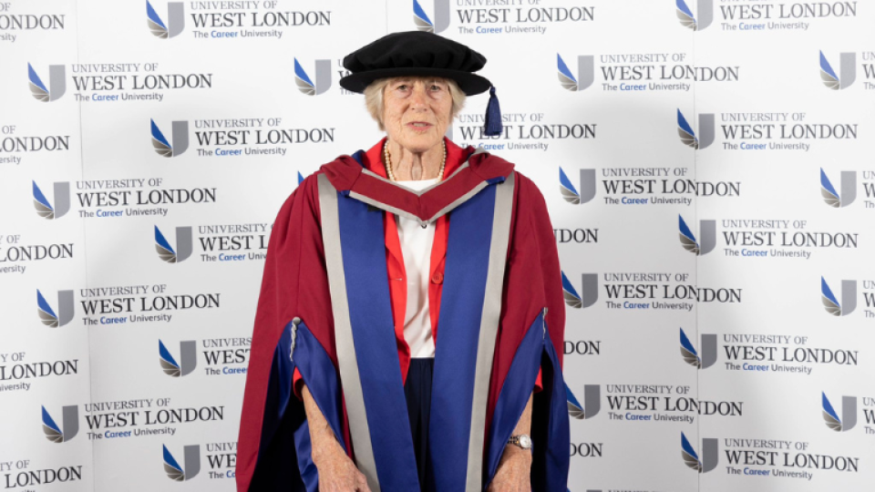 Jean Sykes MBE is wearing a gown and hat as an honoree graduate