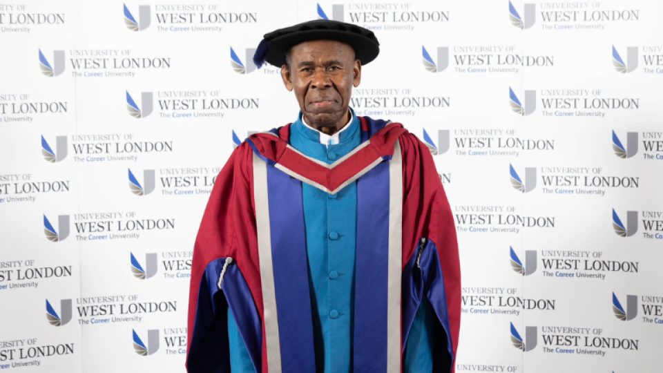 Augustine John is wearing a gown and hat as an honoree graduate