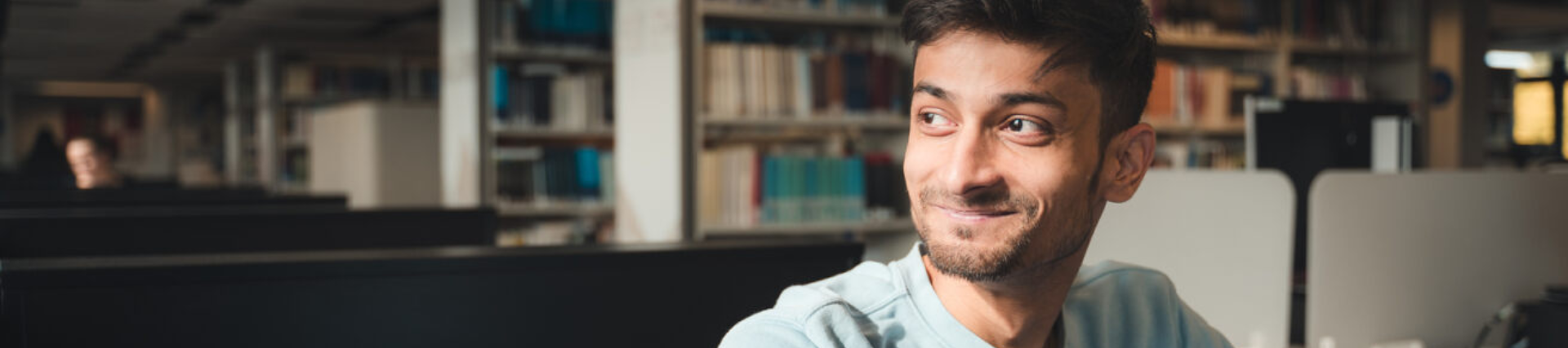 A University of West London student smiling sat in the Paul Hamlyn Library