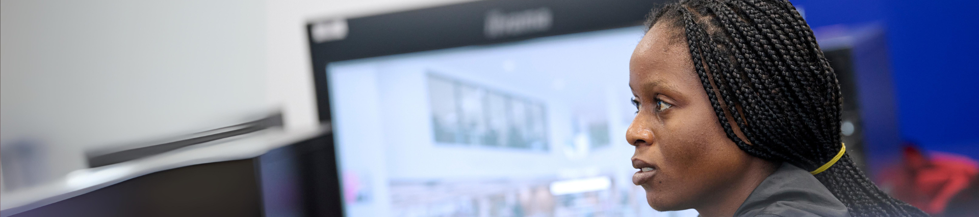 A student looking ahead in a computer lab with a monitor screen behind her.