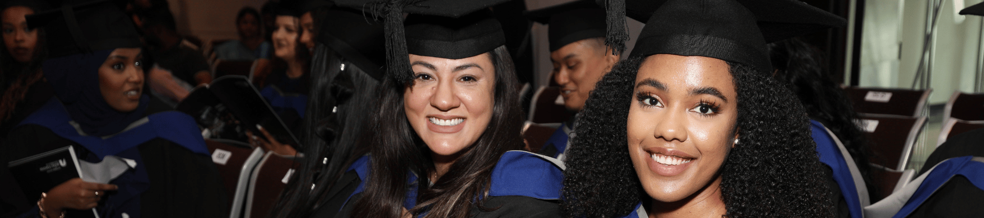 Two students sat at a graduation ceremony wearing gowns.