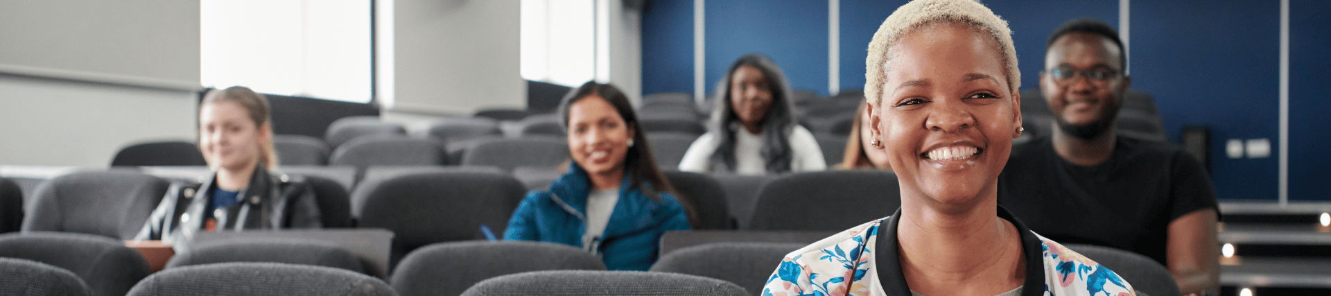 A woman smiling whilst at her laptop during a lecture at William Barry theatre.