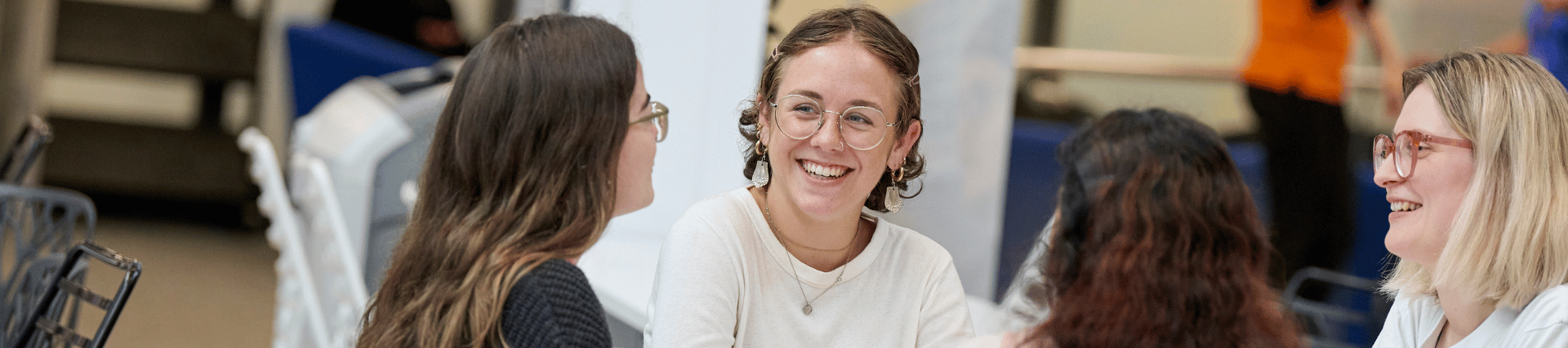 Four students chatting together as a group, two are visibly smiling.