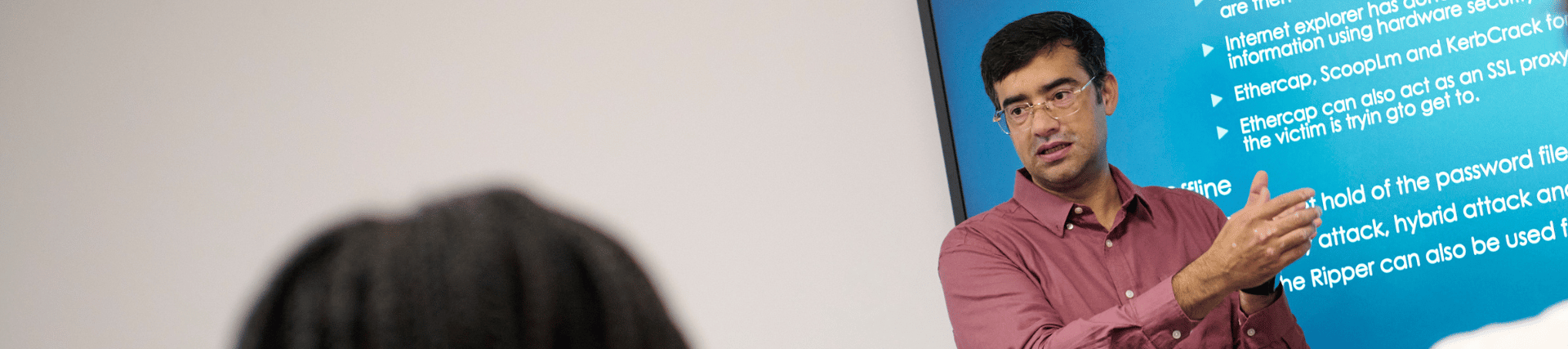 A lecturer doing a presentation at the front of a lecture room to a group of students.