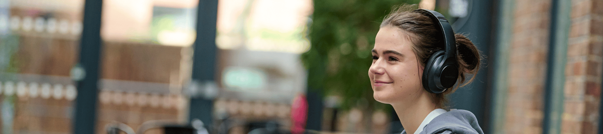 A student smiling with headphones on whilst seated outside the Student Union.