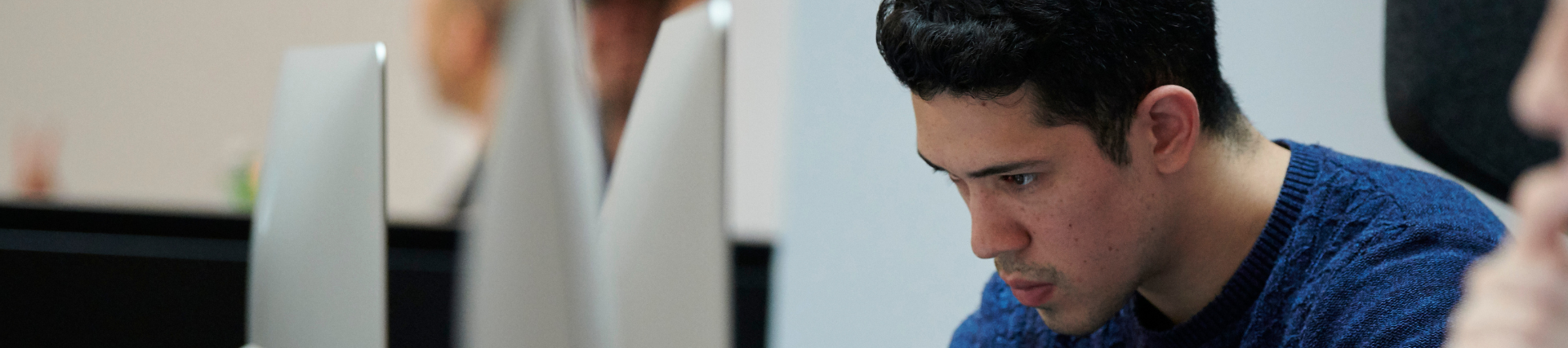 A student working at a computer, looking towards the screen and wearing a blue top.